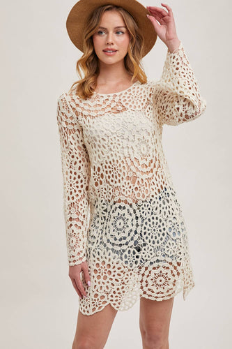 model with wavy dark blonde hair and wearing brown hat, cream crochet dress with swim suit underneath. Crochet pattern is floral.